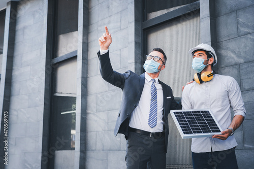 Working in the newnormal, the project engineer and the team leader wear masks. and consulting on the building's solar cell system.engineers team discuss the use of solar energy in modern buildings. photo