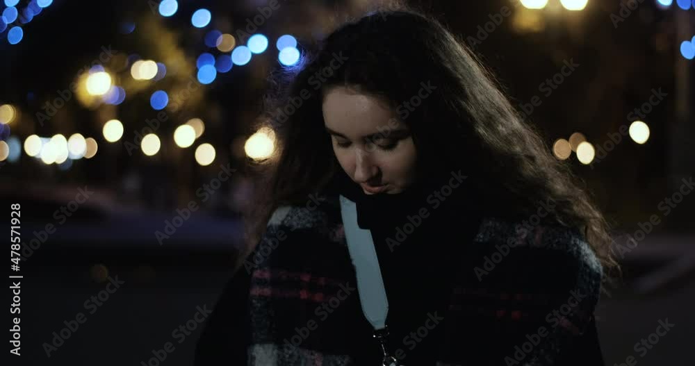 Shy modest young girl with long abundant wavy brown hair walks around the city at night. Girl looks into the camera and smiles shyly Shy modest young girl with long abundant wavy brown hair walks around the city at night. Girl looks into the camera and smiles shyly