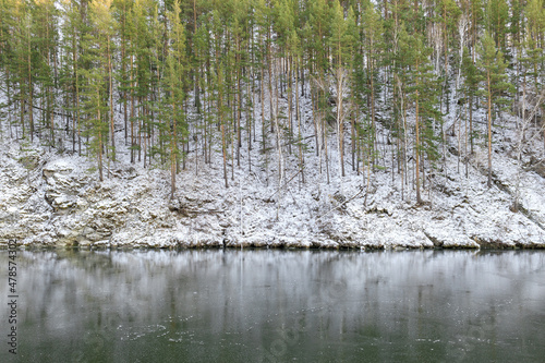 the river is covered with ice in winter, pines and birches grow on the slope