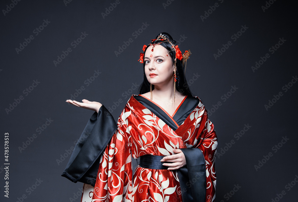 Beautiful young woman in red traditional Chinese costume showing something on empty hand Beautiful young woman in red traditional Chinese costume showing something on empty hand