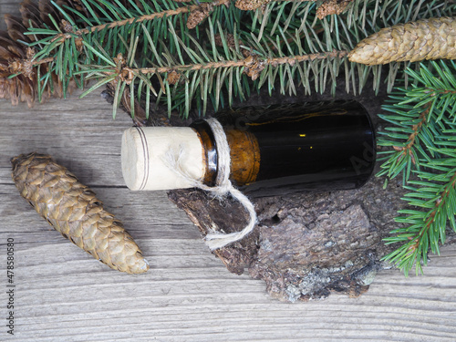 Fresh spruce twigs, big and small fir cones, bark, oil, tincture extract in a bottle on a wooden table, flat layout, top view. Coniferous plant picea abies for use in herbal alternative medicine
