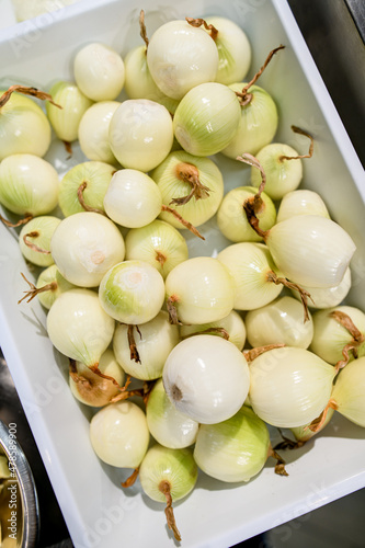 top view of a white tray with many peeled onions photo