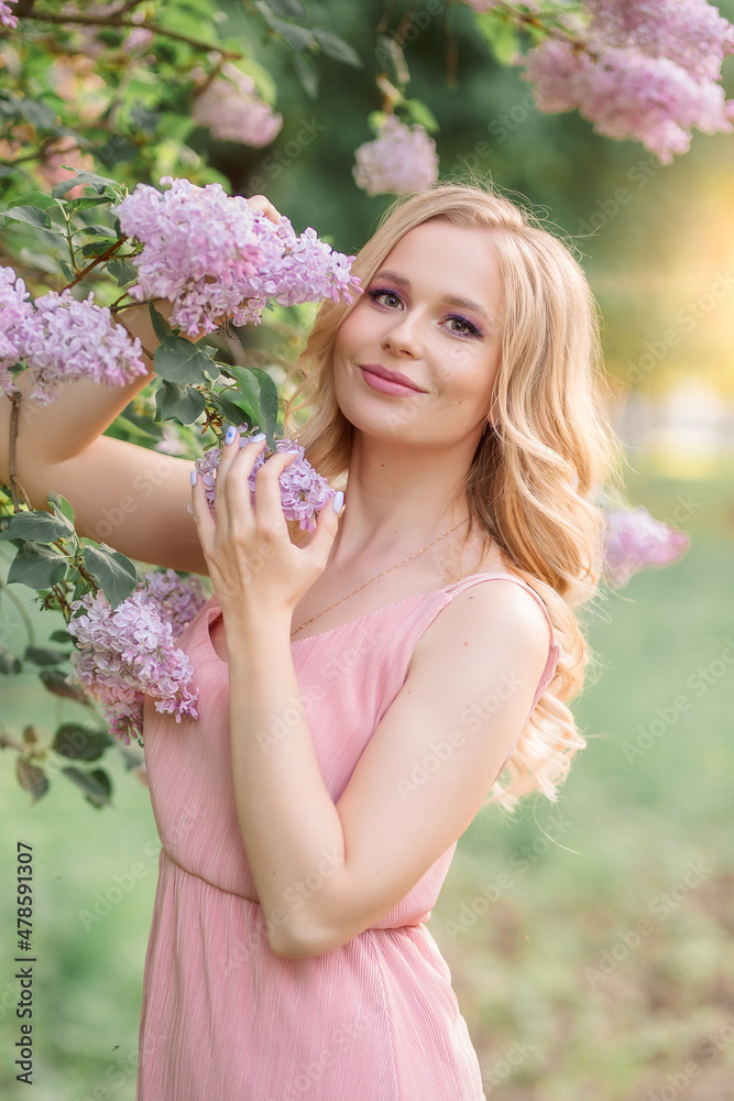 a girl with blonde hair in a pink dress stands next to a branch of lilac a girl with blonde hair in a pink dress stands next to a branch of lilac