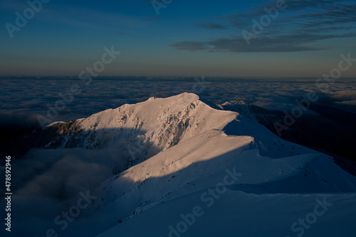 aerial view of the snow-covered mountain range surrounded by clouds against background of sky