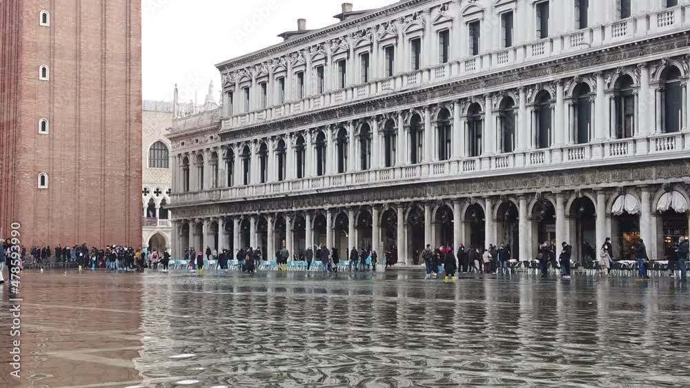 Venice, Italy - January 2022 - San Marco square submerged by high water on a sunny day while tourists are having fun with colored boots Venice, Italy - January 2022 - San Marco square submerged by high water on a sunny day while tourists are having fun with colored boots