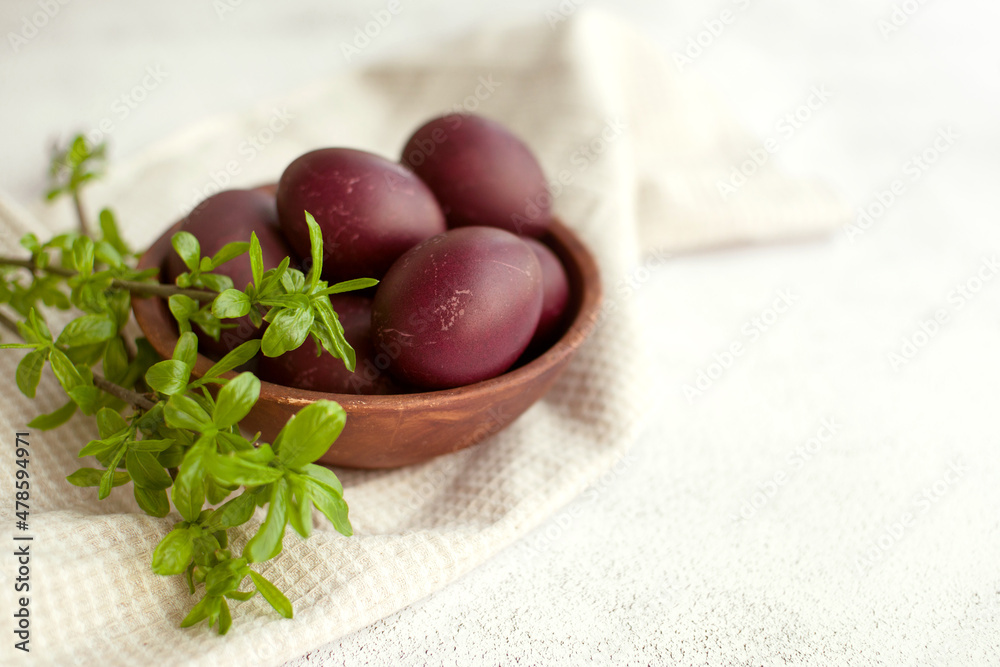 Easter burgundy eggs in a clay plate on a white napkin, decorated with green willow branches on a light background, soft selective focus, copy space. Festive background with Easter symbols Easter burgundy eggs in a clay plate on a white napkin, decorated with green willow branches on a light background, soft selective focus, copy space. Festive background with Easter symbols