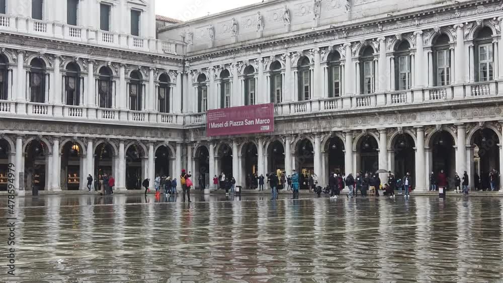 Venice, Italy - January 2022 - San Marco square submerged by high water on a sunny day while tourists are having fun with colored boots Venice, Italy - January 2022 - San Marco square submerged by high water on a sunny day while tourists are having fun with colored boots