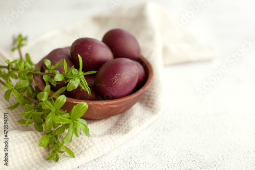 Easter burgundy eggs in a clay plate on a white napkin, decorated with green willow branches on a light background, soft selective focus, copy space. Festive background with Easter symbols