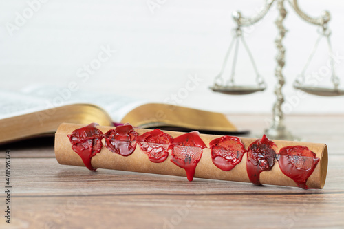 A closeup of an ancient closed scroll with seven seals on a wooden table with Holy Bible Book and old weighing scales against a white background. Christian biblical concept of Revelation's prophecy.