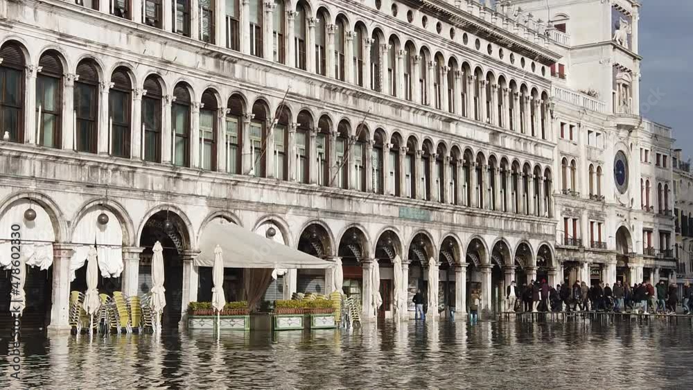Venice, Italy - January 2022 - San Marco square submerged by high water on a sunny day while tourists are having fun with colored boots Venice, Italy - January 2022 - San Marco square submerged by high water on a sunny day while tourists are having fun with colored boots