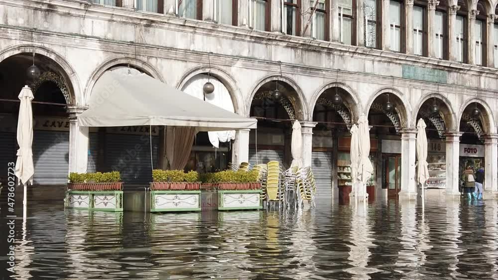 Venice, Italy - January 2022 - San Marco square submerged by high water on a sunny day while tourists are having fun with colored boots Venice, Italy - January 2022 - San Marco square submerged by high water on a sunny day while tourists are having fun with colored boots