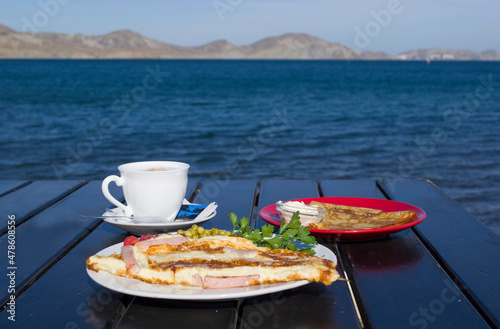 Breakfast in a cafe with a sea view. Coffee in a white cup and pancakes with sour cream on a red plate.