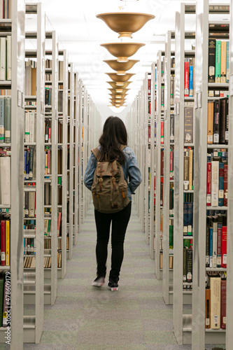 Tela Figura feminina de costas andando por corredor de livros de uma biblioteca