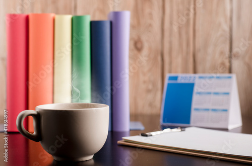 Cup of coffee or tea with hot steam in the morning  books with lgtbi flag colors  on the desk.