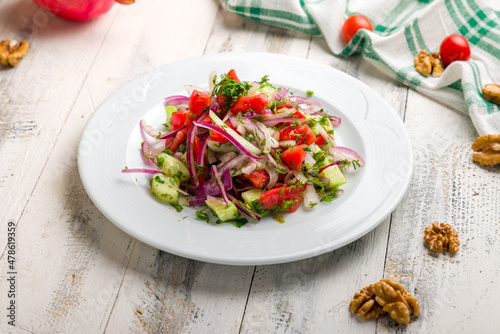 Vegetable salad with tomatoes and cucumbers and red onion on white wooden table