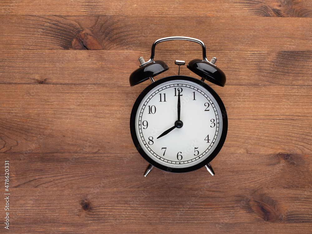 Black retro alarm clock closeup top view on wooden background. Time, deadline and morning routines concept