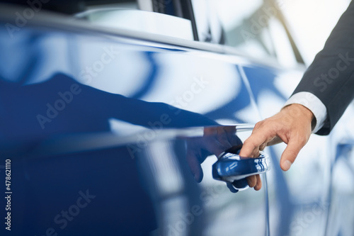 Businessman in suit opening door of his new blue car after successful purchase at salon. Close up of male hand on auto handle. Dealership concept.