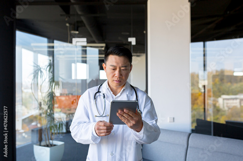 Serious Asian doctor, uses a tablet computer, the man works in a modern clinic