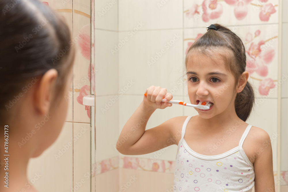 A cute European girl brushes her teeth while looking at her reflection in the mirror. Oral hygiene. A cute European girl brushes her teeth while looking at her reflection in the mirror. Oral hygiene.