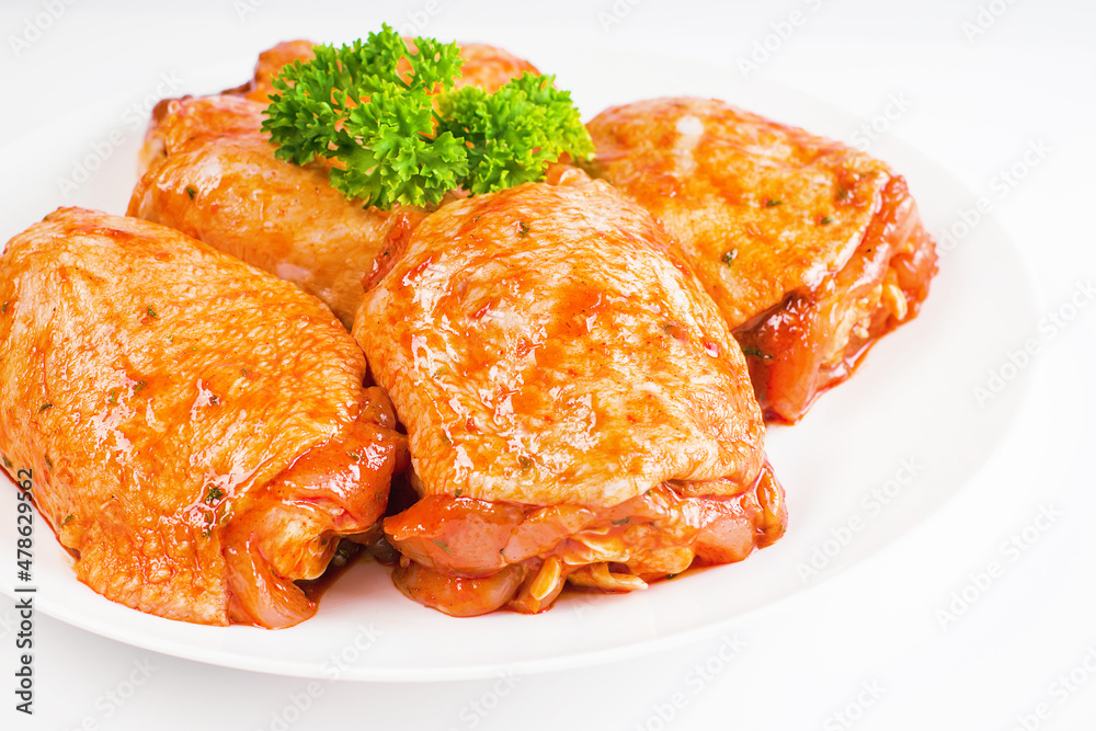 Raw marinated in red sauce chicken thighs on a white plate, on a white isolated background. Top of view.Isolated object, copy space.Raw chicken marinated. Chicken semi-cooked thighs.