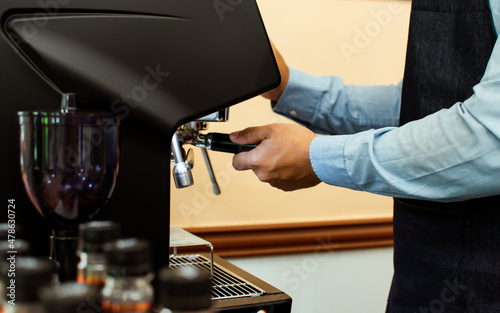 Selective focus and close up on barista's hands preparing coffee for customers and using equipment, pressing machine for brewing in indoor cafe shop. Business and Beverage Concept.