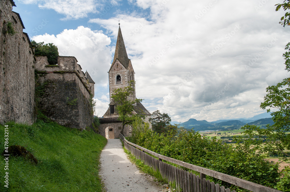 A tall church tower with a clock and an access path and wall defenses at the old Hochosterwitz Castle in Carinthia, Austria.