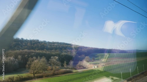 Hills and meadows forests seen through large glass windows of a fast train with reflection in int of front seat passenger