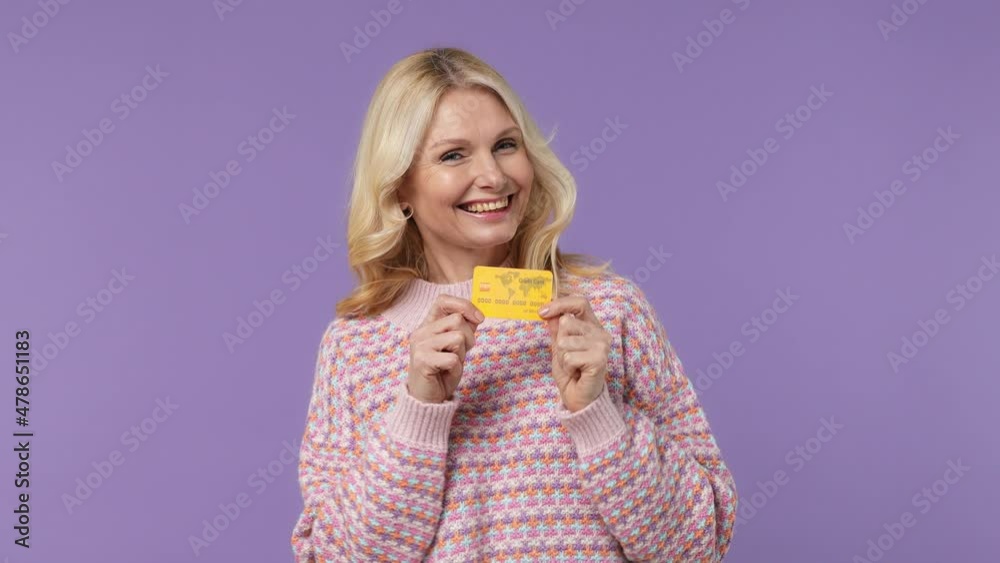 Satisfied elderly blonde woman lady 40s years old in warm shirt point index finger on mockup plastic credit bank card showing thumbs up isolated on plain pastel light purple background studio portrait Satisfied elderly blonde woman lady 40s years old in warm shirt point index finger on mockup plastic credit bank card showing thumbs up isolated on plain pastel light purple background studio portrait