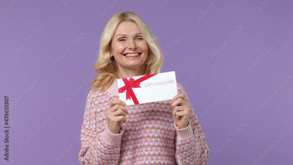 Surprised happy elderly blonde woman lady 40s years old in warm shirt pointing on gift certificate voucher for store do winner gesture isolated on plain pastel light purple background studio portrait Surprised happy elderly blonde woman lady 40s years old in warm shirt pointing on gift certificate voucher for store do winner gesture isolated on plain pastel light purple background studio portrait