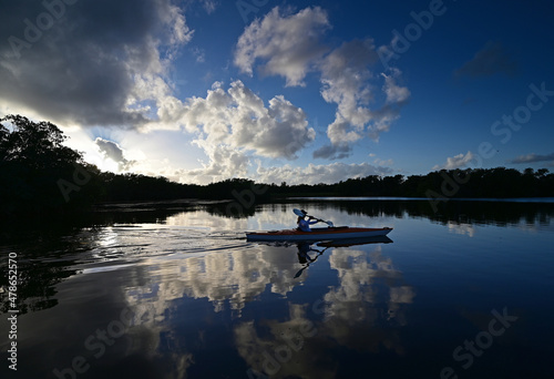 Woman kayaking on Paurotis Pond in Everglades National Park, Florida under afternoon winter cloudscape reflected in water.
