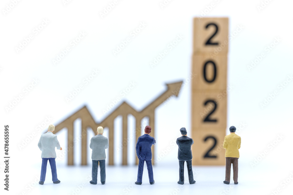 2022 New Year and Business Planning Concept. Closeup of group of businessman miniature figures standing and looking to wooden arrow chart sign and stack of wooden number block on white background. 2022 New Year and Business Planning Concept. Closeup of group of businessman miniature figures standing and looking to wooden arrow chart sign and stack of wooden number block on white background.