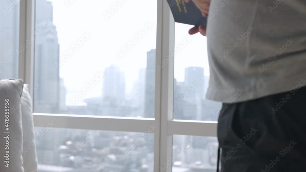 an asian man reading a booking in living room with background of the city center with skyscraper through big window an asian man reading a booking in living room with background of the city center with skyscraper through big window