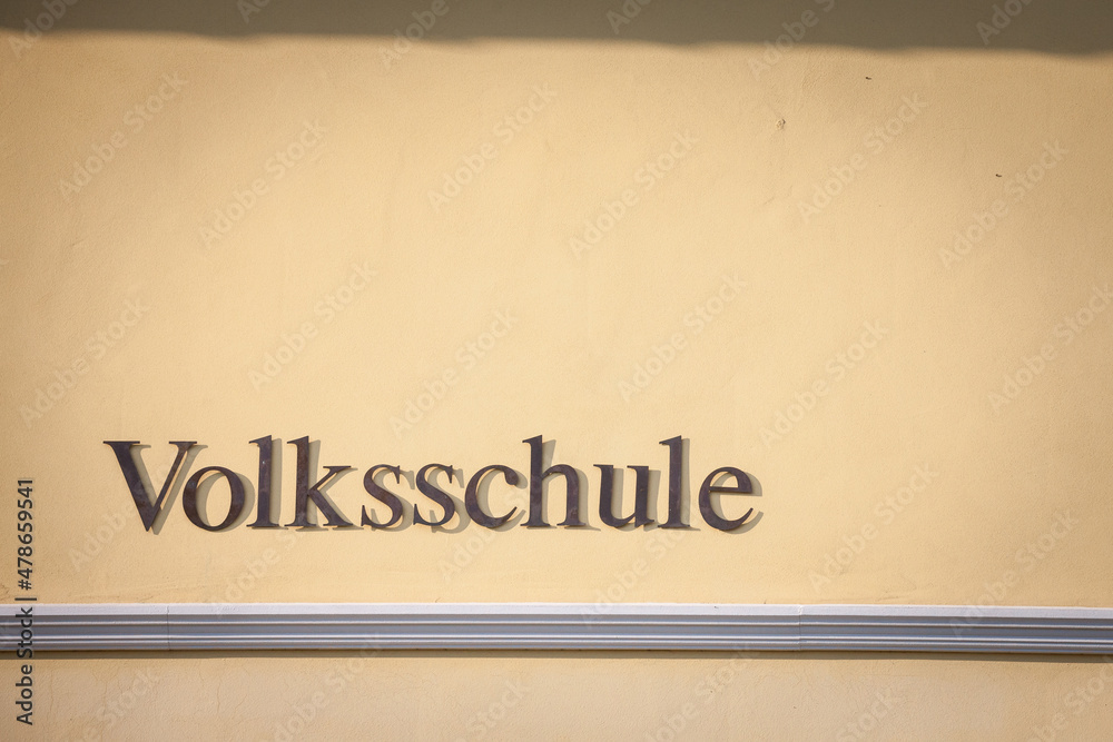 Obraz premium Sign indicating Volksschule, meaning in german People's school, on a building in Austria. Volksschule in Germany, Austria and Switzerland englobes primary and secondary school levels for students