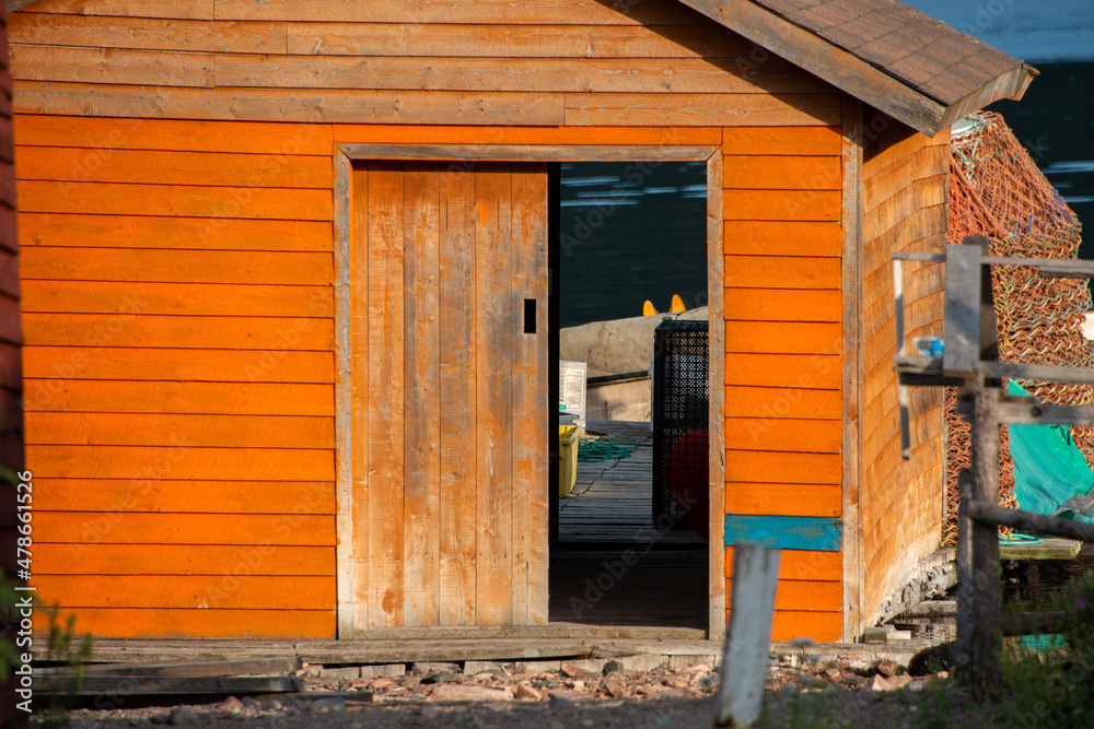 Orange wooden fishing shed for storing fishing gear and boats. The building  has a worn wooden