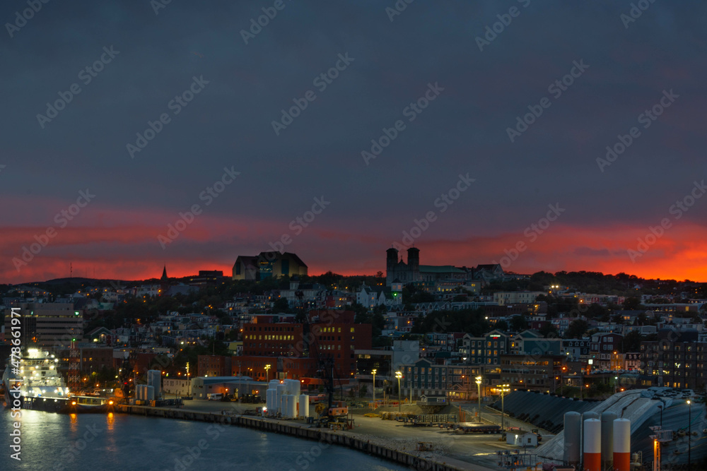 St. John's, Newfoundland, Canada-January 2022: A nighttime view of downtown St. John's skyline with an orange glow in the sky at sunset. There are oil and gas supply boats docked at the harbour. 
