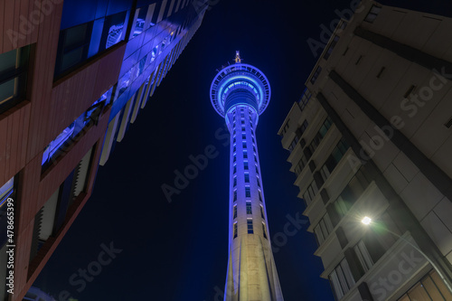 Fotografia Night scene tall circular tower illuminated blue viewed through strings of decorative fairy lights