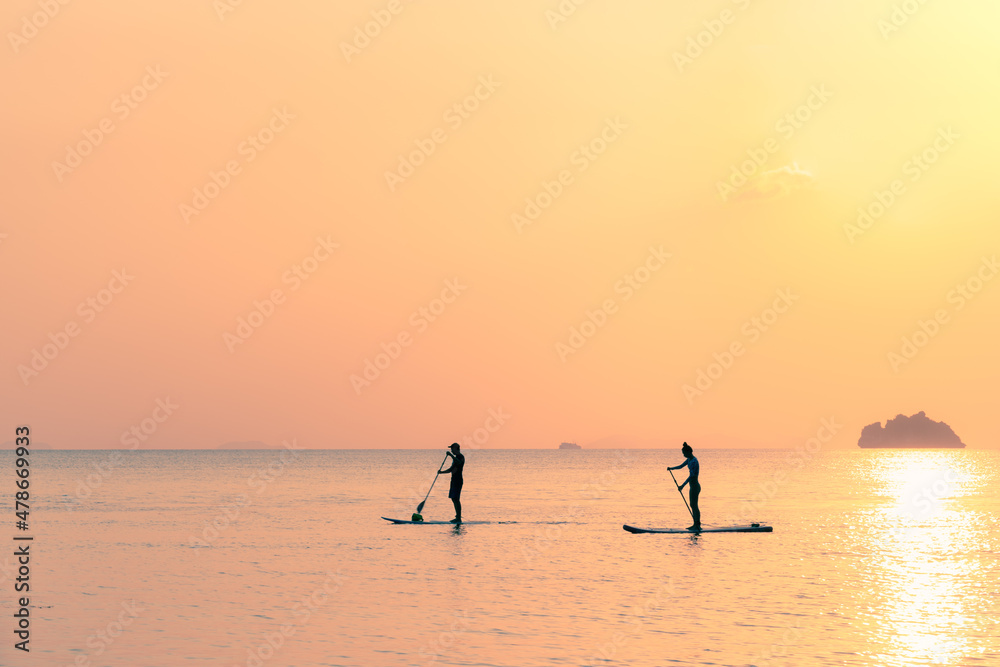 A couple on stand up paddle boards floats in the sea against the backdrop of island at sunset A couple on stand up paddle boards floats in the sea against the backdrop of island at sunset