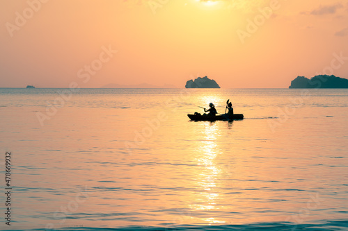 A couple swims in the sea on a kayak against the backdrop of island at sunset