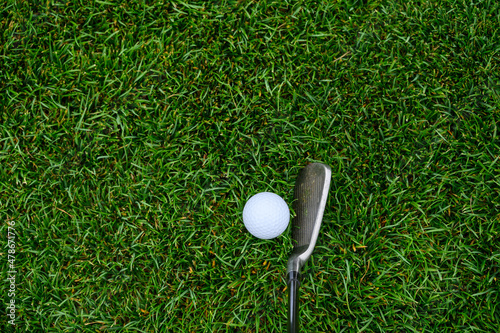 Lush green golf course grass in the rough, with a white golf ball and an iron clubhead ready to play 