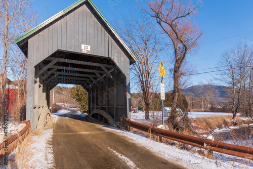 Looking East as the sun gets sets in the west Best's wooden covered bridge in winter located in west Windsor Vermont blue-gray wood stained bridge spanning the mill creek