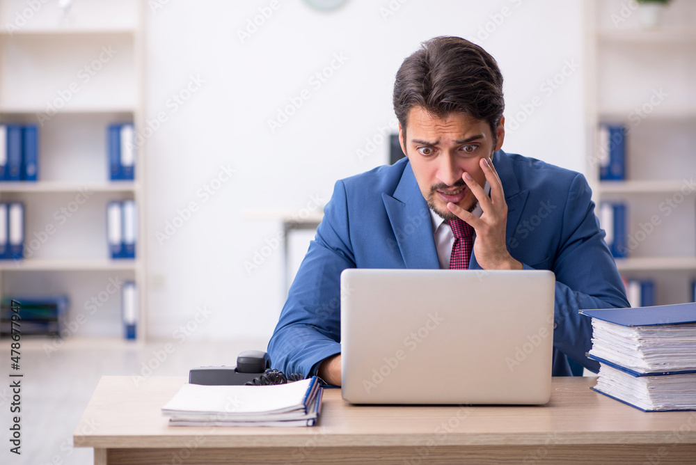 Young male employee unhappy with excessive work in the office Young male employee unhappy with excessive work in the office