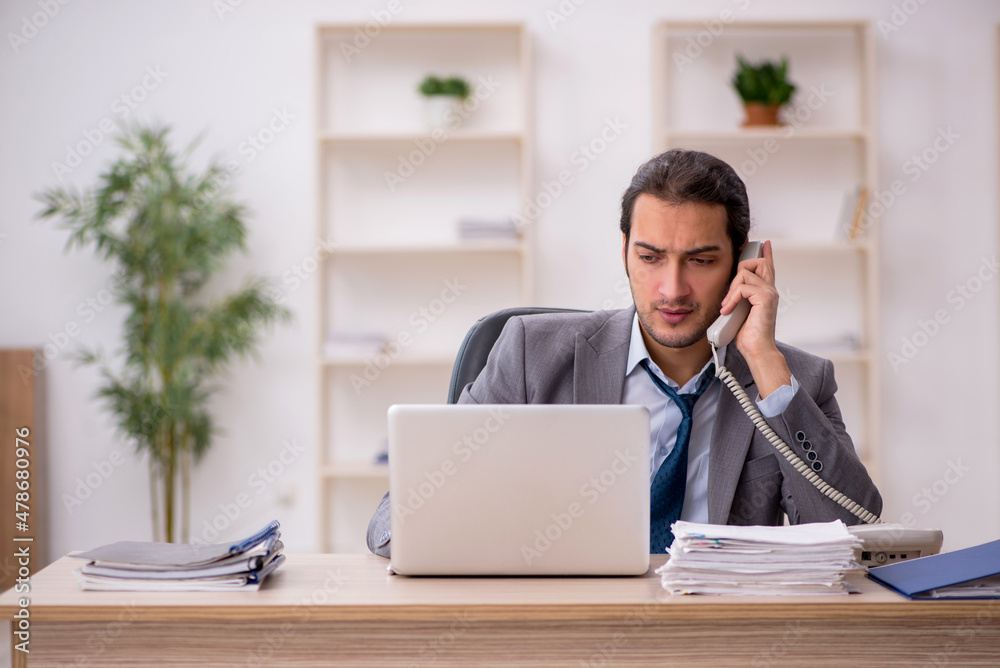 Young male employee unhappy with excessive work in the office Young male employee unhappy with excessive work in the office