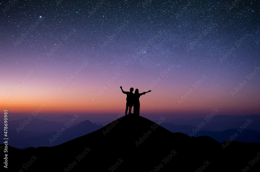 Silhouette of young couple standing with both hands above your head watched the star and milky way on top of the mountain. Couple enjoyed traveling and was successful when he reached the summit.