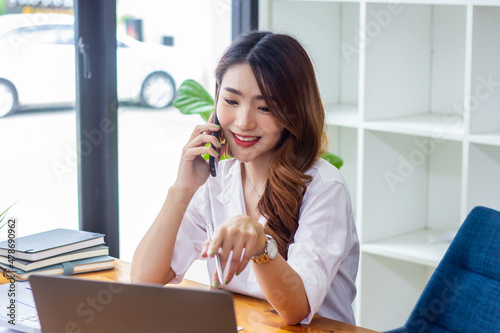 Businesswoman discussing company sales data last year on the phone, woman sitting in a chair looking at financial documents, accountant checking company numbers, concept of modern business people.