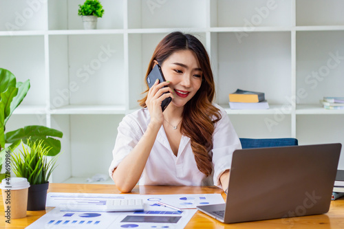 Businesswoman discussing company sales data last year on the phone, woman sitting in a chair looking at financial documents, accountant checking company numbers, concept of modern business people.