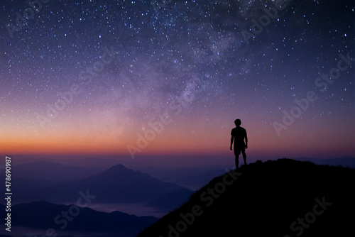 Fototapeta Silhouette of young man standing and watched the star, milky way and night sky alone on top of the mountain
