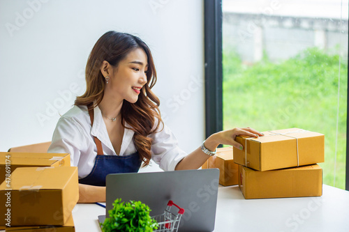 An online business owner checks the name and address of a customer ordering a company product, Cropped photo of a woman checking and writing the name on a parcel for delivery at an online sale office.