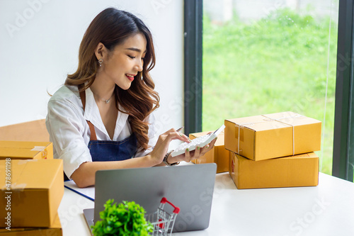 An online business owner checks the name and address of a customer ordering a company product, Cropped photo of a woman checking and writing the name on a parcel for delivery at an online sale office.