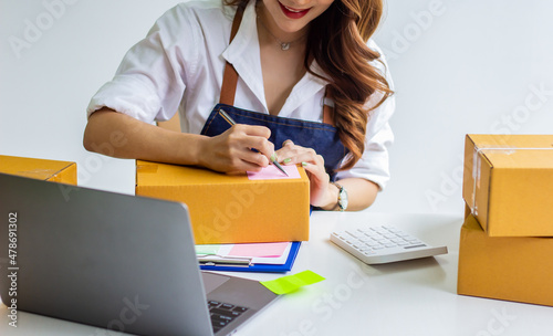 An online business owner checks the name and address of a customer ordering a company product, Cropped photo of a woman checking and writing the name on a parcel for delivery at an online sale office.