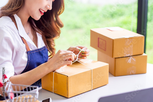 Small business owners look at company's past online sales, cropped image of woman tying up her own shipping box for delivery at online sales office, merchandising concept and modern businessman.